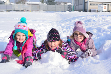 Three little girls playing in the snow in a sunny winter day