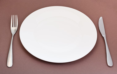 white porcelain plate with fork and knife on brown