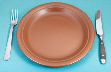 brown ceramic plate with fork and knife on green