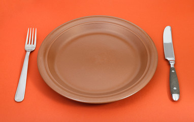 brown ceramic plate with fork and knife set on red