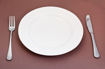 empty white plate with fork and knife set on brown