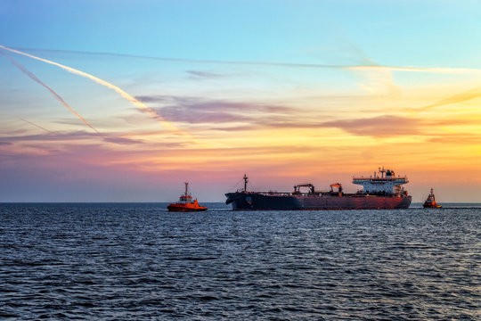 Tanker ship with escorting tugs on sea at sunrise.