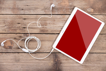 Tablet computer with earphones against wooden background