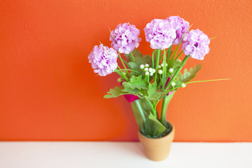pink artificial flower made from cloth on bright orange wall, wa
