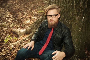 Naklejka na ściany i meble Blond beard fashion man sitting near a tree