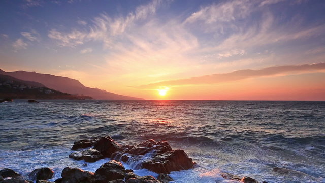Waves break about stones at sunrise over the sea