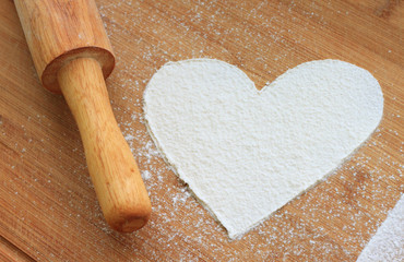 heart from white flour on wooden background and rolling-pin