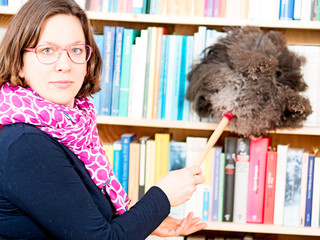 Frau staubt Bücherregal ab