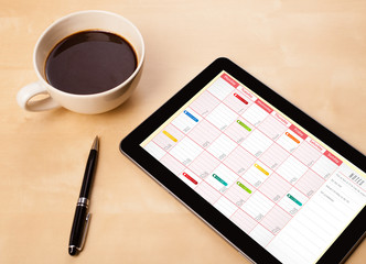 Tablet pc showing calendar on screen with a cup of coffee on a d