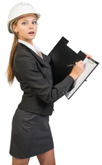 Businesswoman wearing hard hat, writing on clipboard