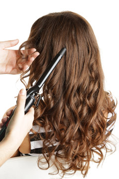Stylist using curling iron for hair curls, close-up, isolated