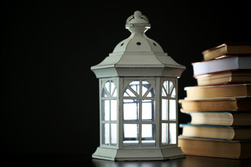 Books and decorative lantern on table and dark background