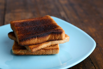 Burnt toast bread on turquoise plate, on wooden table