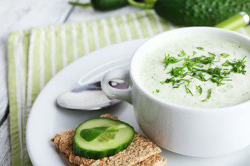 Cucumber soup in bowl on color wooden table background