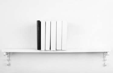 Blank books with black one on bookshelf on white wall
