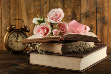 Books with flowers and clock on wooden background