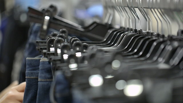 Woman in the store choosing jeans hanging on racks