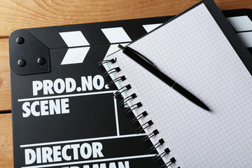 Movie clapper with notebook and pen on wooden background