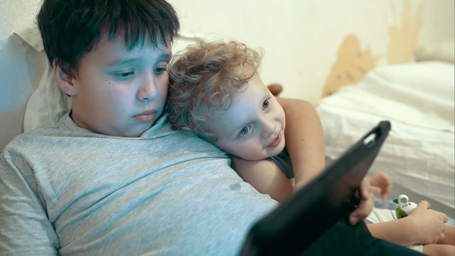 Two brothers with pad lying in bed. Entertainment with tablet PC