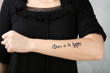 Female arm with tattoo on light background