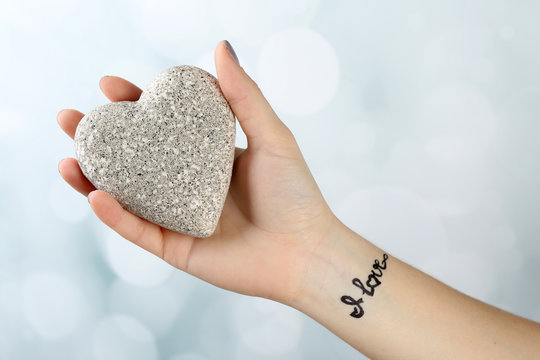 Naklejki Female arm with tattoo holding decorative heart on light background