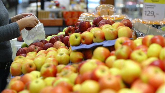 Woman in the supermarket putting apples in plastic bag