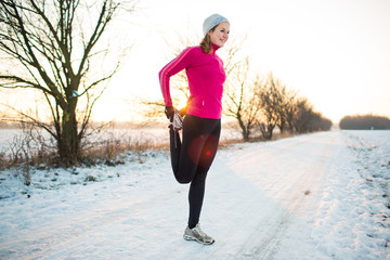 Young woman stretching while running outdoors on a cold winter