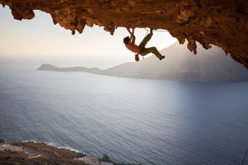 Rock climber climbing along roof in cave at sunset - obrazy, fototapety, plakaty