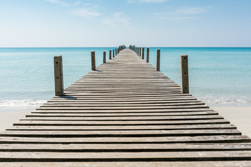 Wooden bridge on the beach to the sea in blue sky.