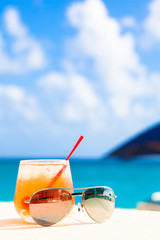 glass of chilled cocktail rum punch and sunglasses on table near the beach