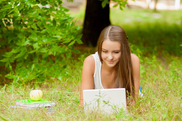 Teen girl works with the laptop on the grass near the tree