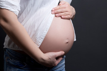 close up of pregnant woman's belly over grey