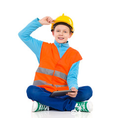 Little construction worker sitting with a digital tablet