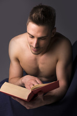 Shirtless athletic young man reading big book