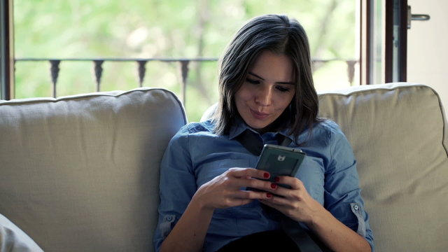 Happy, pretty businesswoman using smartphone sitting on sofa 