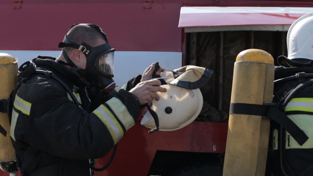 Firefighters wear gas masks and uniforms while standing by fire