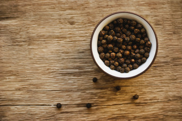 Black pepper in the ceramic dish on the wooden background