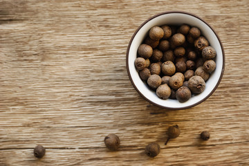 Allspice in the ceramic dish on the wooden background