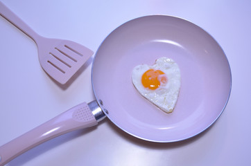 Heart shaped egg on a pink pan with a pink spatula.