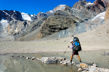 Man with backpack resting on trekking pole moves a river
