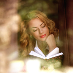 Beautiful girl reading a book indoors, the view through window