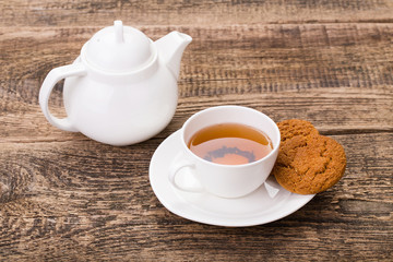 ivory tea cup with sweet cookie, and kettle on wooden palette