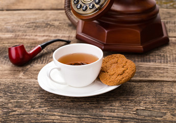 ivory tea cup with sweet cookie, old telephone and tobacco pipe