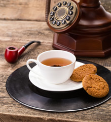 ivory tea cup with sweet cookie, old telephone and tobacco pipe