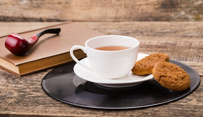 ivory tea cup with sweet cookie, book and tobacco pipe on wooden