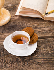 Image of ivory tea cup with sweet cookie, book, pen on wooden pa