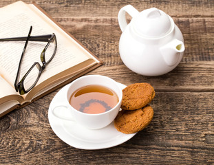 ivory tea cup with sweet cookie, glasses and book on wooden pale