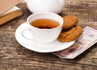 ivory tea cup with sweet cookie, and dollar money on wooden pale