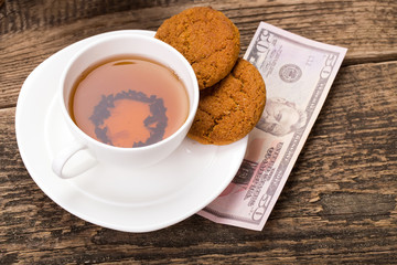 ivory tea cup with sweet cookie, and dollar money on wooden pale