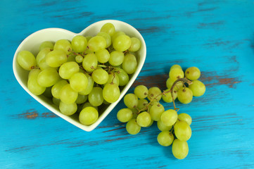 Green grapes in heart shaped bowl on a turquoise wood background